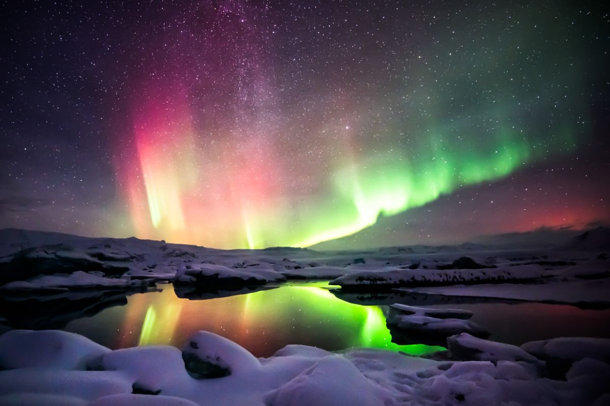 Northern lights glowing green and pink over a snowy lagoon in Iceland
